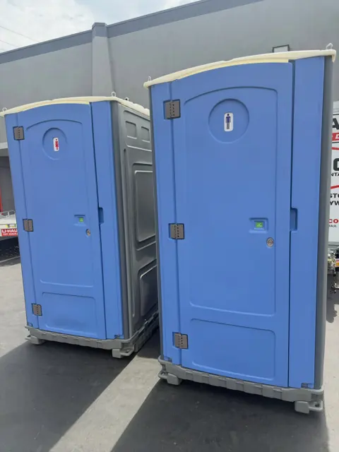 A blue and a gray porta potty set side by side on asphalt