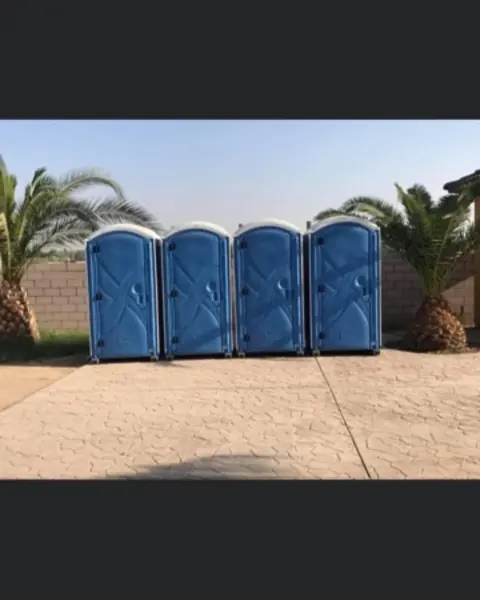 Row of four blue porta potties lined up on pavement for an event