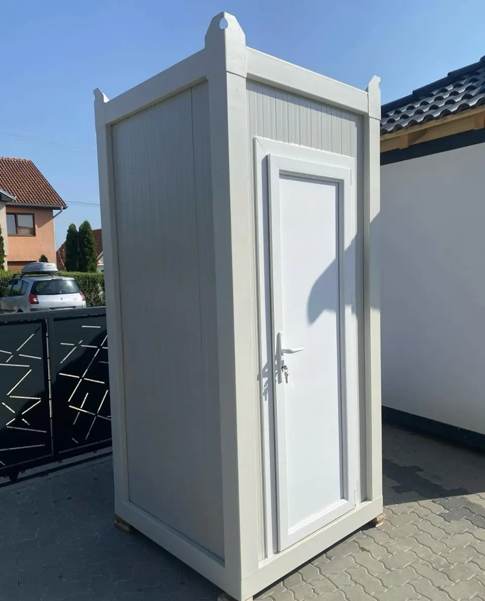 White hard-wall restroom cabin beside a home