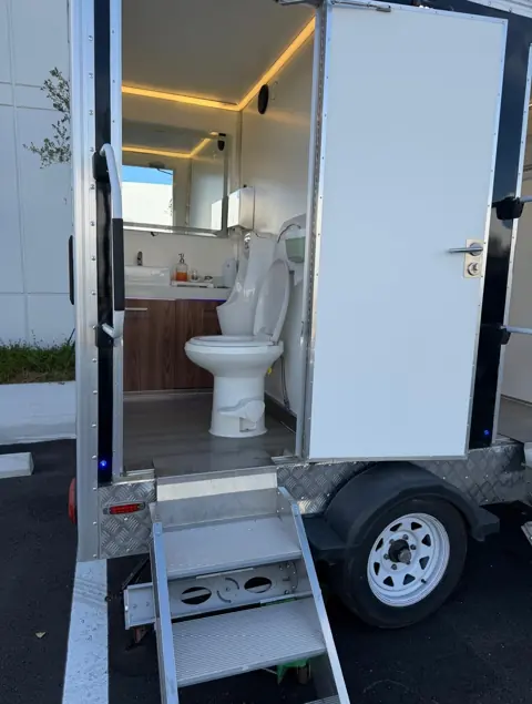 Open door of a restroom trailer showing the toilet and vanity