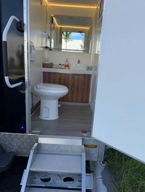 Restroom trailer stall with flushing toilet and wood-look floor