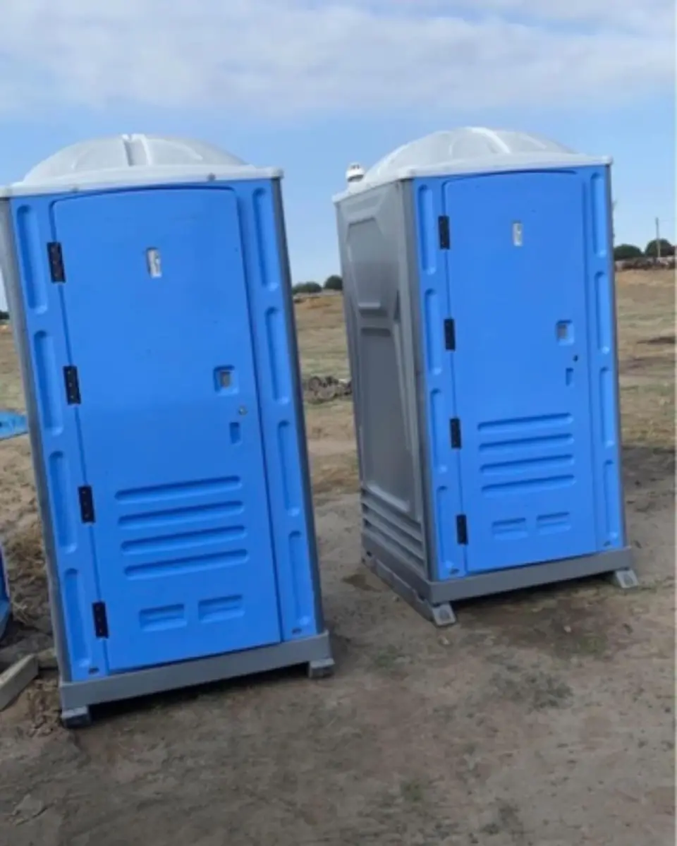 Two blue standard porta potties set on a dirt lot at a construction site