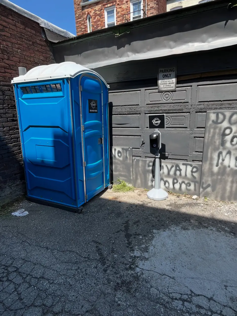 Blue standard porta potty placed on an alley pad behind a building